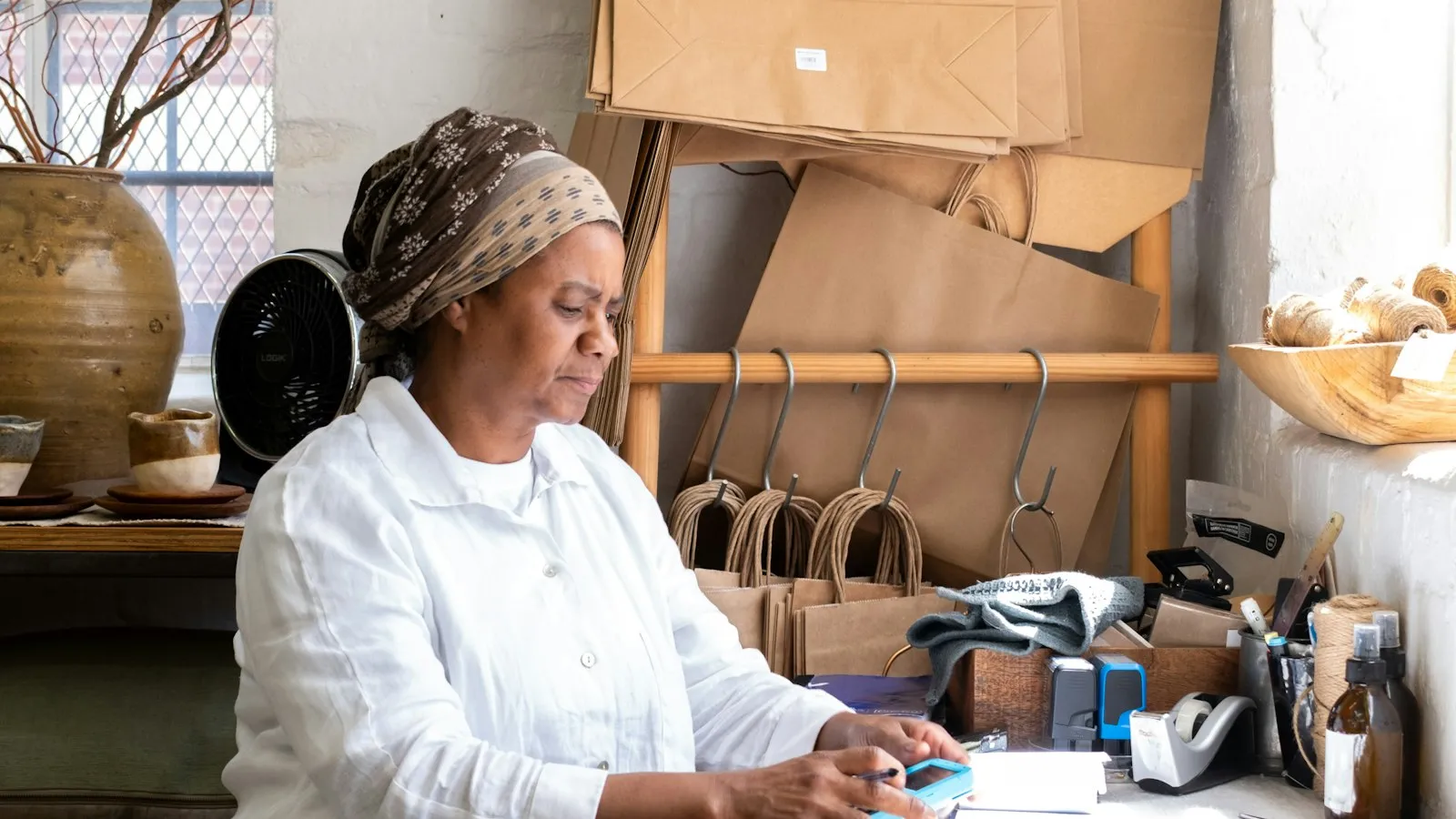 Small business owner preparing an order at a desk beside paper bags and packaging